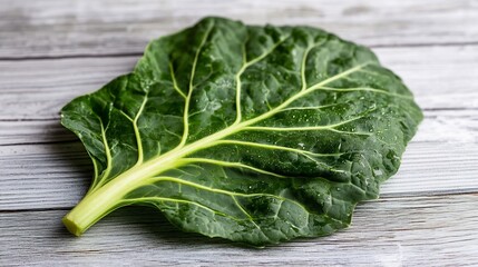 Close up shot of a single collard green leaf with visible veins and water droplets highlighting the...
