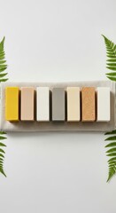 Various Natural Soap Bars in Earthy Tones Arranged on Fabric with Green Ferns on White Background