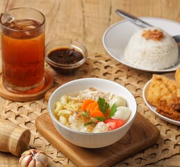 Sop ayam kampung. A bowl of free-range chicken soup with macroni, shredded chicken, sliced ​​carrots, sliced ​​wood ear mushrooms and boiled quail eggs accompanied by rice, fried food, soy sauce and a