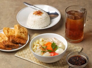 Sop ayam kampung. A bowl of free-range chicken soup with macroni, shredded chicken, sliced ​​carrots, sliced ​​wood ear mushrooms and boiled quail eggs accompanied by rice, fried food, soy sauce and a