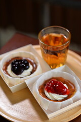 Burnt cheesecake with whipped cream and strawberry jam, served on a wooden tray with a glass of warm tea. Cozy dessert time in soft natural light.
