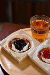 Burnt cheesecake with whipped cream and strawberry jam, served on a wooden tray with a glass of warm tea. Cozy dessert time in soft natural light.