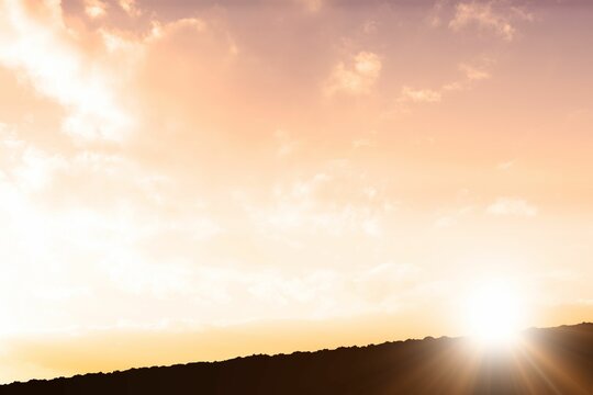 Fototapeta Sun is rising above ridge silhouette in flat design, casting glowing rays through scattered clouds