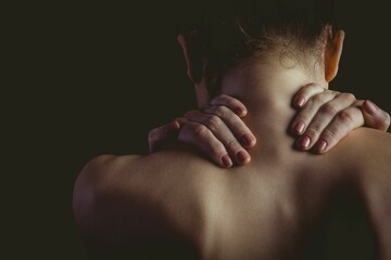 woman is placing hands on bare shoulders in dark studio portrait, highlighting skin texture
