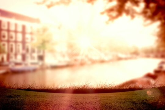 Fototapeta Flat design showing sunlit canal water flowing past grassy bank, brick facade, foliage, lens flare
