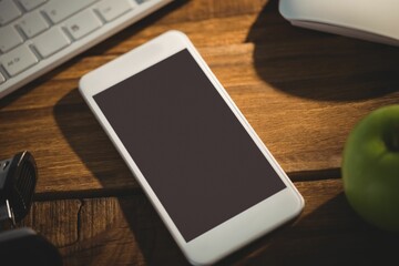 Flat design is showing white smartphone resting on wooden desk with keyboard, mouse, green apple