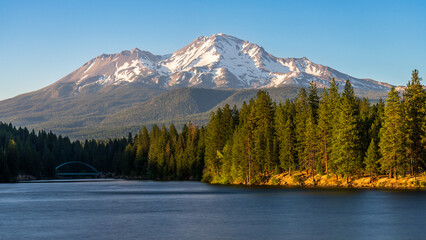 Mount Shasta and Lake Siskiyou, summer evening, with warm lights on the mountain and surrounding forest. California, USA.