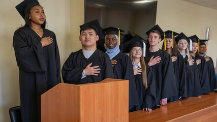 Graduates stand proudly at the ceremony with their hands over their hearts. 