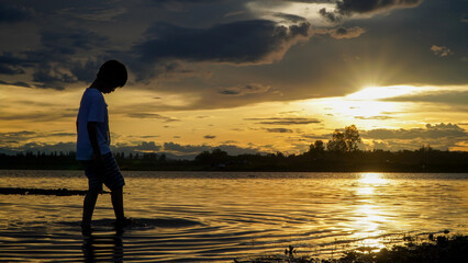 silhouette of asian boy playing in the water at sunset.Thai