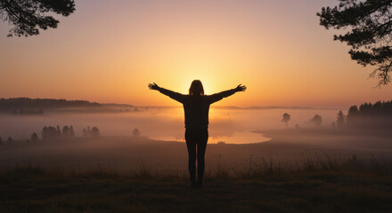 Silhouette of Person with Arms Outstretched at Sunrise Over Misty Landscape