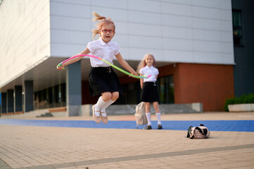 girl jumping rope schoolyard fun happiness. young girl skipping rope while friend watches outside modern school. joyful play, childhood adventure, vibrant student life captured