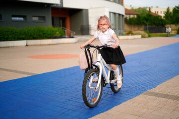 little girl riding bicycle on blue pathway. child wearing glasses and school uniform biking...
