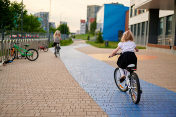mother and daughter cycling together on colorful city path, exploring urban environment. scenic...