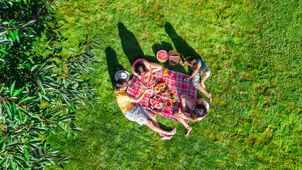 Happy family with children having picnic in park, parents with kids sitting on garden grass and...
