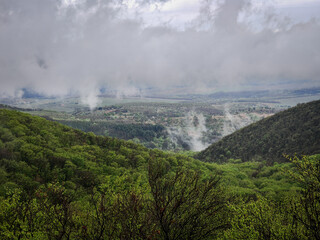 A distant view from Buzgó-kő towards the northern hills and a valley town. Morning fog rolls through the green forest