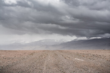 Panorama of mountain peaks with snow and glaciers, a landscape in the highlands of the Tien Shan in Pamir in cloudy weather with clouds and rain, high-mountain steppe and mountains in the background