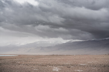 Panorama of mountain peaks with snow and glaciers, a landscape in the highlands of the Tien Shan in Pamir in cloudy weather with clouds and rain, high-mountain steppe and mountains in the background