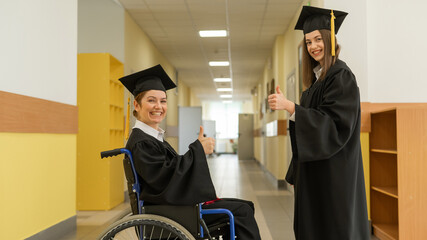 Happy young woman and woman in wheelchair in graduate gown with diploma in hands. Inclusive...