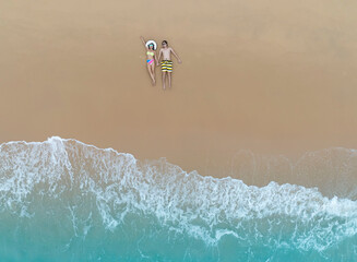 Aerial view of young asian couple relaxation sunbath as lying on the beach in Maldives