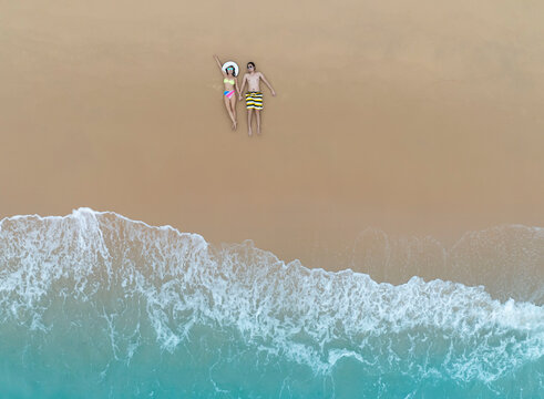 Aerial view of young asian couple relaxation  sunbath as lying on the beach  in Maldives