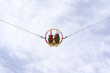 Launching a catapult in an amusement park with two young women sitting in a ball against a light cloudy sky, their long hair fluttering in the wind. An exciting attraction for adults and teenagers.