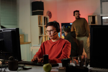 Young adult man wearing headset operating computer in scam call center foreground, man standing in...