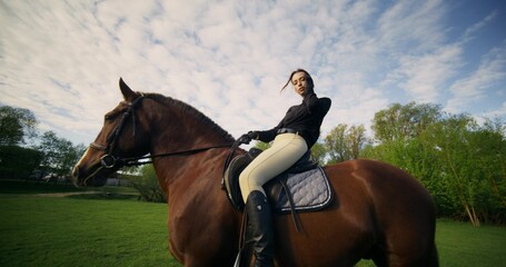 A stylish woman poses sitting on a horse on a cloudy day at a farm