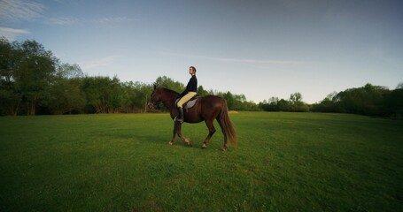 A stylish woman poses sitting on a horse on a cloudy day at a farm