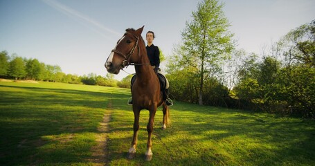 A stylish equestrian poses looking at the camera while sitting on a horse on a sunny day