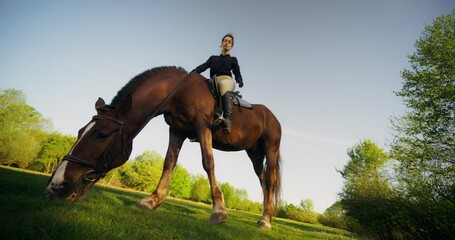 Stylish equestrian posing looking at the camera while sitting on a horse on a sunny day, bottom view