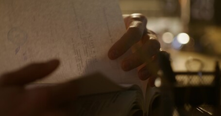 The man flips through the pages while sitting at the table. Close-up of his hands, unrecognizable...