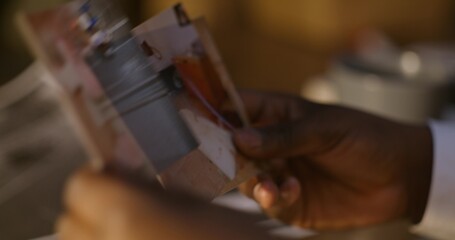 The detective examines photographs from the scene of the attack. Close-up of his hands,...