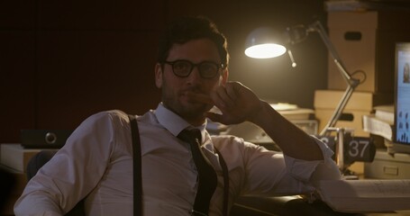 A stylish man is sitting at his desk. He looks around. Detective in the office