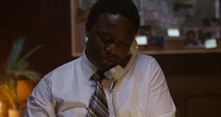 A detective is talking on the phone while sitting at a desk in the office. He's smiling.