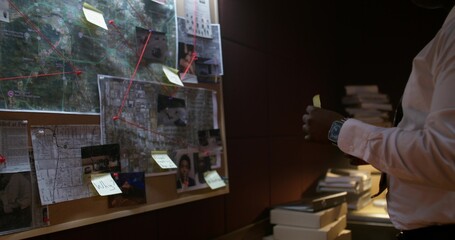 The detective puts sticky notes on a board with photos. Solving a crime