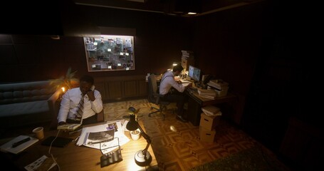 Working in the police office. One of the detectives is on the phone, the other is using a computer.