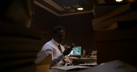 A detective listens to an audio recording on a dictaphone. He works in the office next to his colleague.