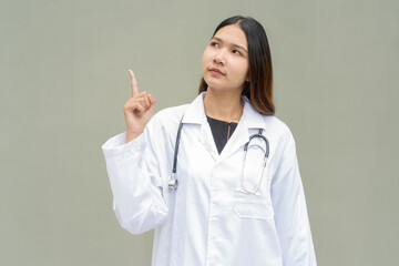 Young Asian woman doctor wearing white lab coat and stethoscope pointing finger