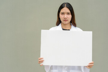 Young woman doctor wearing white lab coat and stethoscope holding empty placard with copy space