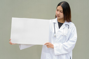 Young woman doctor wearing white lab coat and stethoscope holding empty placard with copy space