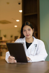Young woman doctor wearing white lab coat and stethoscope sitting hospital library reception