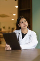 Young woman doctor wearing white lab coat and stethoscope sitting hospital library reception