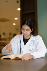 Young woman doctor reading book while sitting in hospital library