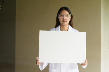Scientist woman wearing lab coat and goggles holding placard with copy space