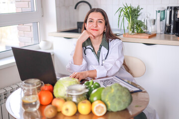 Nutritionist working with clients at a table full of fresh vegetables and fruits using a laptop and...