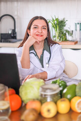 Close-up of a nutritionist at a table full of fresh vegetables and fruits using a laptop and a...