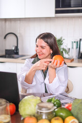 nutritionist conducting a consultation at a table with fruits and vegetables using a laptop and a...