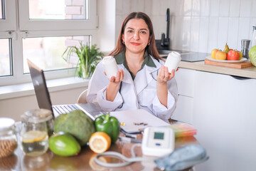 A female nutritionist in a white coat shows jars of dietary supplements against a background of...