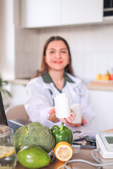 Dietitian in a white coat holds jars of dietary supplements and provides nutritional advice against...