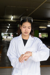 Scientist woman wearing lab coat and goggles outside building using smarwatch